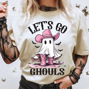 Może przedstawiać: Biała koszulka z nadrukiem ducha w r&oacute;żowym kowbojskim kapeluszu i butach. Na koszulce widnieje napis "Let's Go Ghouls".