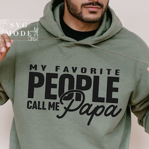 Peut inclure: Un sweat &agrave; capuche vert olive avec le texte noir "MY FAVORITE PEOPLE CALL ME Papa". Le sweat &agrave; capuche a un cordon de serrage et une poche avant. L'image comprend &eacute;galement le texte "SVG MODE" dans le coin sup&eacute;rieur gauche.