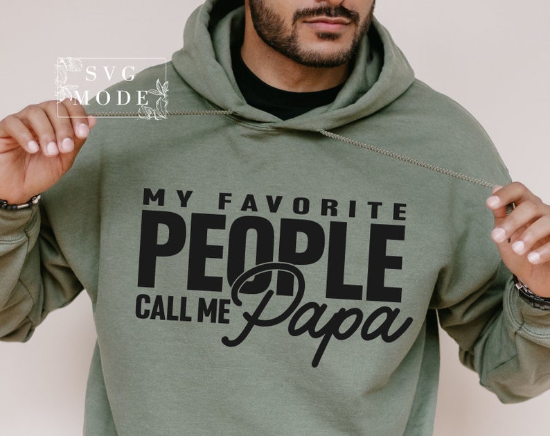 Peut inclure: Un sweat &agrave; capuche vert olive avec le texte noir "MY FAVORITE PEOPLE CALL ME Papa". Le sweat &agrave; capuche a un cordon de serrage et une poche avant. L'image comprend &eacute;galement le texte "SVG MODE" dans le coin sup&eacute;rieur gauche.