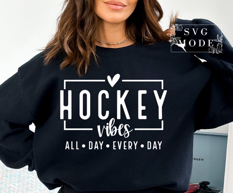 Puede incluir: Sudadera negra con texto blanco que dice "Hockey vibes all day every day" con un peque&ntilde;o coraz&oacute;n sobre la palabra "Hockey".