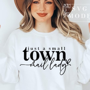 Peut inclure: Sweat-shirt blanc avec un texte noir qui dit "just a small town mail lady" avec un petit graphique de c&oelig;ur.