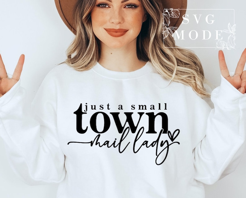 Peut inclure: Sweat-shirt blanc avec un texte noir qui dit "just a small town mail lady" avec un petit graphique de c&oelig;ur.