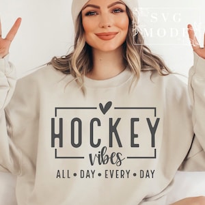 Puede incluir: Una sudadera beige con el texto "HOCKEY vibes ALL DAY EVERY DAY" en un rect&aacute;ngulo negro con un peque&ntilde;o coraz&oacute;n arriba.