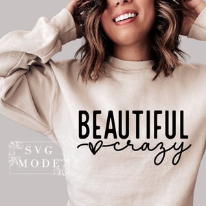Pode incluir: Uma camisa de moletom bege com o texto "BEAUTIFUL crazy" em letras pretas. Um pequeno cora&ccedil;&atilde;o &eacute; desenhado entre as palavras.