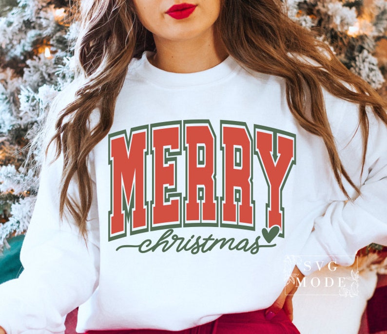 May include: White sweatshirt with the text "MERRY" in red block letters with a green outline. Below, the word "christmas" is written in a cursive font, with a green heart. The sweatshirt is a festive holiday design.