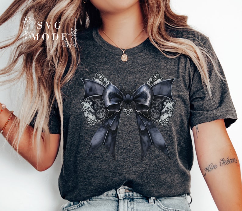 May include: A dark gray t-shirt with a black and white lace bow design. The bow has a heart in the center.