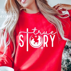 May include: Red sweatshirt with white text that reads "true story" and a white silhouette of the nativity scene.