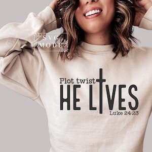 May include: A beige sweatshirt with the text "Plot twist HE LIVES Luke 24:23" printed on the front. The text is in black and features a black cross.