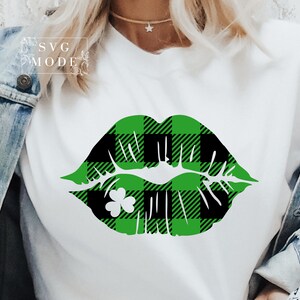 May include: A white t-shirt with a green and black buffalo plaid lip print with a shamrock in the center.