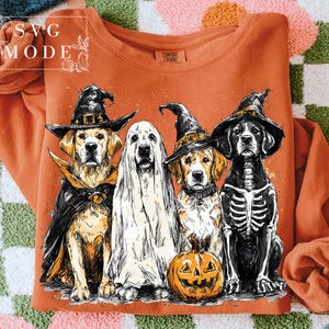 May include: Orange sweatshirt featuring a Halloween-themed graphic of four dogs dressed in costumes: a witch, a ghost, a witch, and a skeleton. A carved pumpkin is in front of the dogs. The text "SVG MODE" is in the upper left corner.