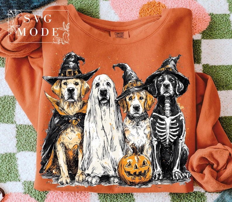 May include: Orange sweatshirt featuring a Halloween-themed graphic of four dogs dressed in costumes: a witch, a ghost, a witch, and a skeleton. A carved pumpkin is in front of the dogs. The text "SVG MODE" is in the upper left corner.