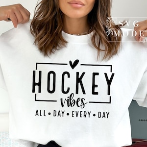 Puede incluir: Sudadera blanca con texto negro que dice "Hockey vibes all day every day" con un coraz&oacute;n sobre la palabra "Hockey".