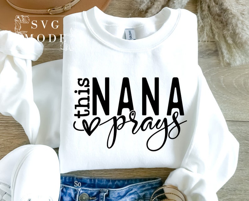 May include: White sweatshirt with black text that reads "this NANA prays" with a heart symbol.