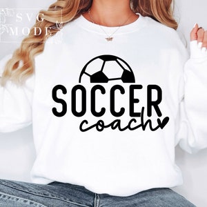 May include: White sweatshirt with a black football graphic and the text "SOCCER coach" with a heart.