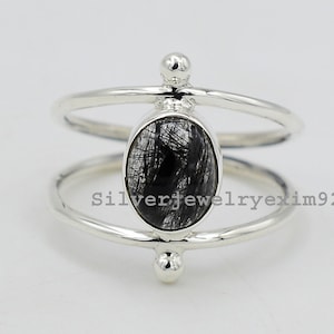 以下が含まれることがあります： 黒い楕円形の宝石がダブルバンドのデザインにセットされたシルバーリング。リングには、石の両側に3つの小さなシルバーボールがあります。