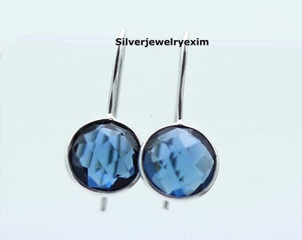 Puede incluir: Un par de pendientes de plata con gotas de piedras preciosas azules. Las piedras preciosas son facetadas y tienen un color azul oscuro.