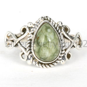 May include: A silver ring with a green gemstone set in a teardrop shape. The ring has a detailed design with intricate swirls and a rope-like border around the stone.