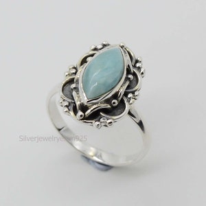 May include: A silver ring featuring a light blue gemstone set within an intricate filigree design.