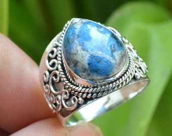 Puede incluir: Un anillo de plata con una piedra preciosa azul y blanca engastada en un diseño de filigrana decorativo.