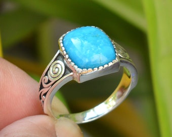 Puede incluir: Un anillo de plata con una piedra turquesa cuadrada engastada en un bisel decorativo. La banda está adornada con un diseño de espiral.