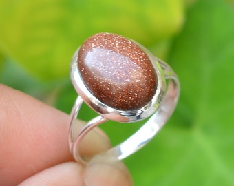 May include: A silver ring with a brown oval-shaped gemstone. The gemstone has a sparkly, glittery texture.