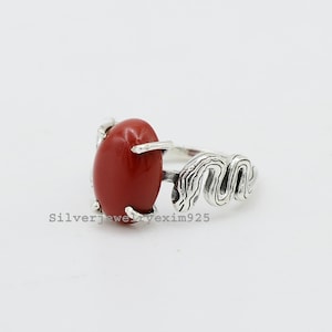 May include: A silver ring with a red oval gemstone and a wavy, snake-like band.