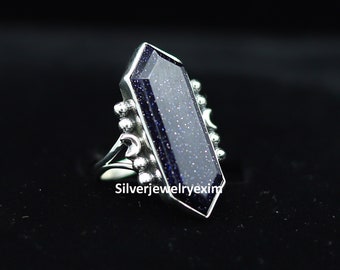 Puede incluir: Un anillo de plata con una gran piedra preciosa rectangular azul. La piedra preciosa tiene una superficie texturizada y brillante. El anillo tiene una banda decorativa con pequeñas cuentas.