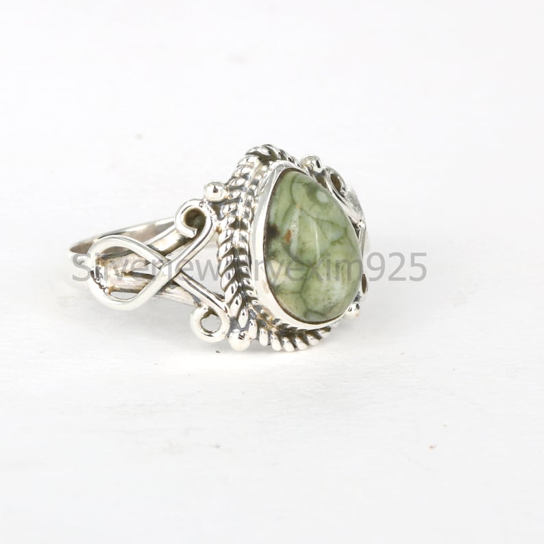 May include: A silver ring with a green and brown teardrop-shaped stone set in a detailed silver setting.