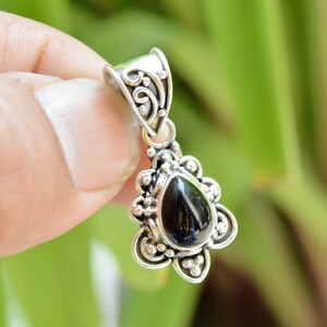 Puede incluir: Un colgante de plata con un dise&ntilde;o adornado y una piedra preciosa negra en forma de l&aacute;grima.
