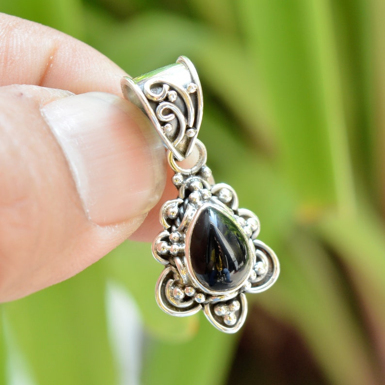 Puede incluir: Un colgante de plata con un dise&ntilde;o adornado y una piedra preciosa negra en forma de l&aacute;grima.