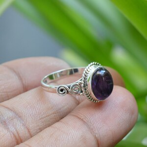 May include: A silver ring with a purple amethyst gemstone. The ring has a twisted band and a detailed setting.