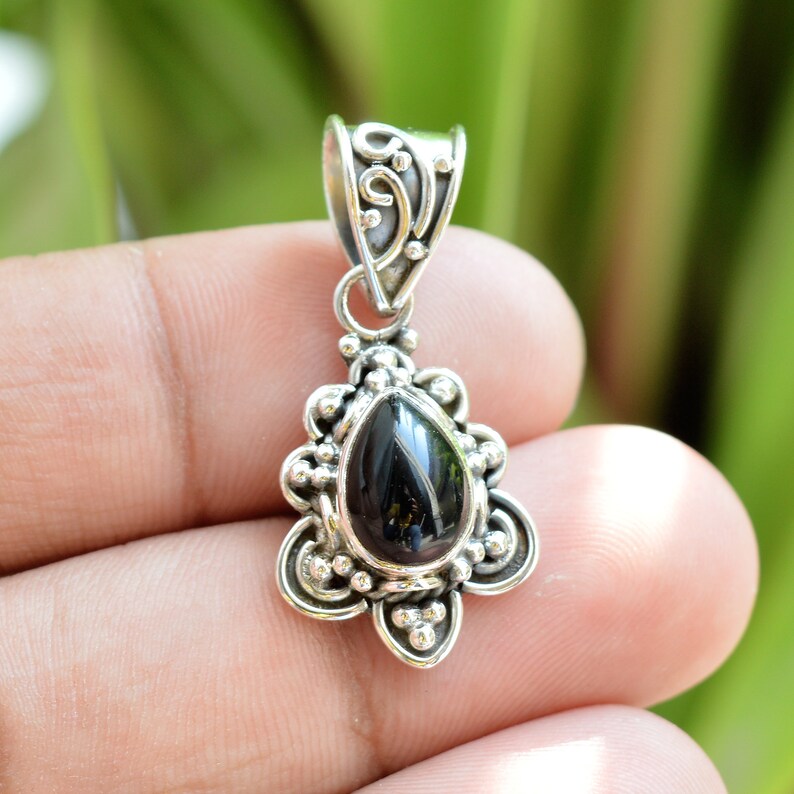 Puede incluir: Un colgante de plata con una piedra preciosa negra en forma de l&aacute;grima. El colgante tiene un dise&ntilde;o detallado y adornado.