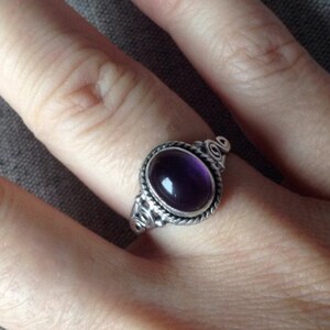 May include: A silver ring with an oval-shaped amethyst gemstone set in a decorative silver bezel. The ring has a twisted silver band.