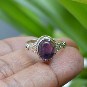 May include: A silver ring with a purple amethyst gemstone set in a decorative swirl design.
