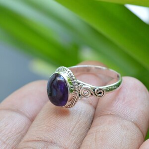 May include: A silver ring with a purple amethyst gemstone set in a decorative bezel. The ring band features intricate scrollwork.