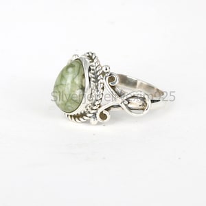 May include: A silver ring with a green and white oval-shaped gemstone. The ring has a detailed design with a twisted rope pattern and a decorative swirl.