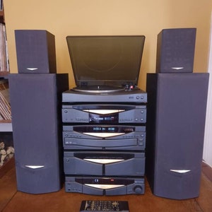 May include: A black stereo system with a turntable, CD player, and cassette player. The system has two speakers on either side. The system has a digital display that reads "DISC 01 01:00".