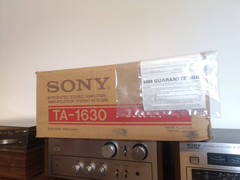 Puede incluir: Una caja de cart&oacute;n marr&oacute;n con las palabras "SONY" y "TA-1630" impresas en ella. La caja es para un amplificador est&eacute;reo integrado. La caja est&aacute; encima de un receptor est&eacute;reo plateado con una placa frontal negra y un sintonizador plateado.