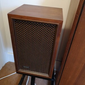 Puede incluir: Un par de altavoces est&eacute;reo vintage de madera con acabado en madera marr&oacute;n y rejilla de altavoz negra. Los altavoces est&aacute;n sobre soportes de metal negro. El altavoz de la izquierda tiene la palabra "SONY" impresa en la parte delantera.