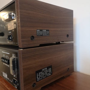 Puede incluir: Un sistema est&eacute;reo vintage con un gabinete de madera. La parte posterior del sistema tiene una etiqueta de precauci&oacute;n que dice "Para evitar descargas el&eacute;ctricas, no retire la cubierta o la parte posterior. No hay piezas reparables por el usuario en el interior. Consulte el servicio t&eacute;cnico a personal de servicio cualificado."