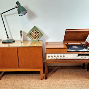 May include: A vintage stereo system with a turntable, amplifier, and speakers. The turntable has a wooden lid that is open, revealing the record player. The amplifier has a wooden cabinet with a white faceplate and several knobs. The speakers are also wooden and have a black grille.