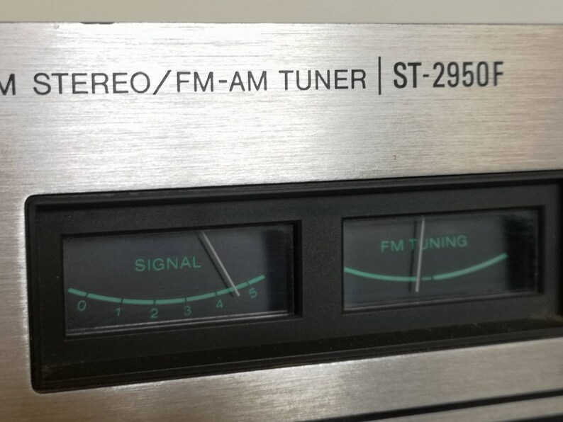 Puede incluir: Primer plano de un sintonizador est&eacute;reo plateado con una placa frontal negra. La placa frontal tiene dos medidores anal&oacute;gicos, uno etiquetado como "SIGNAL" y el otro como "FM TUNING". El sintonizador est&aacute; etiquetado como "M STEREO/FM-AM TUNER | ST-2950F".