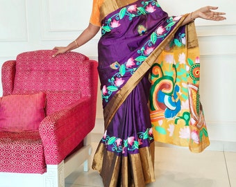 May include: A woman wearing a purple and gold saree with intricate floral embroidery and a yellow blouse. The saree has a colorful design on the pallu.