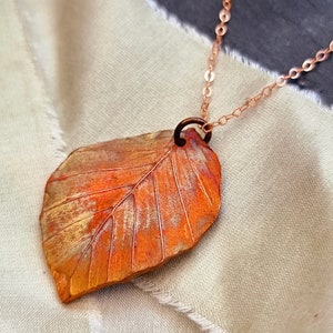 May include: A copper leaf pendant necklace with a delicate chain. The leaf is detailed with veins and has a rustic, oxidised finish.