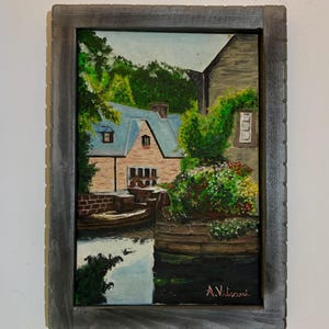 Peut inclure: Peinture à l'huile d'une scène de village pittoresque avec une rivière, des bâtiments et une végétation luxuriante. La peinture est encadrée dans un cadre en bois gris. La signature de l'artiste, "A. Vitrani", est visible en bas à droite.
