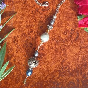 May include: A silver chain necklace with a large silver and gold bead, a white pearl, and smaller silver and blue beads.