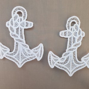 Könnte beinhalten: Zwei weiße Spitzenanker mit einem Seildesign. Die Anker befinden sich auf einem hellbraunen Hintergrund.