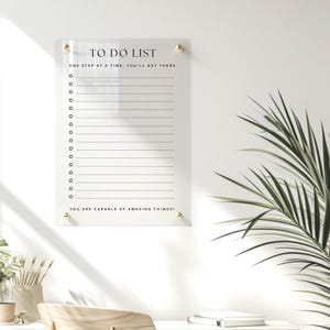 May include: A clear acrylic to-do list board with gold accents and the text "TO DO LIST" at the top. The board has a motivational quote: "ONE STEP AT A TIME, YOU'LL GET THERE" and "YOU ARE CAPABLE OF AMAZING THINGS!"