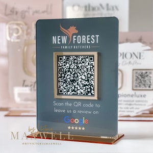 May include: A grey rectangular sign with a gold-framed QR code, promoting Google reviews for "NEW FOREST FAMILY BUTCHERS". The base is a clear, reddish-brown colour. The sign also features the text "Scan the QR code to leave us a review on Google".