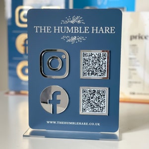May include: A blue sign with the text "THE HUMBLE HARE" and the website address "www.thehumblehare.co.uk". The sign also features silver icons for Instagram, Facebook, and two QR codes.